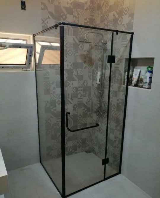 Frameless corner glass shower enclosure with sliding door on marble tiles — BlueCrest